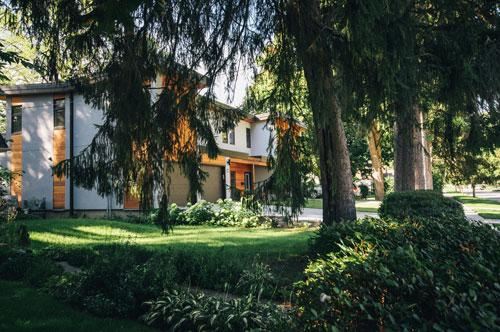 a dark grey and wood house with green grass, partially covered by a large dark green tree.